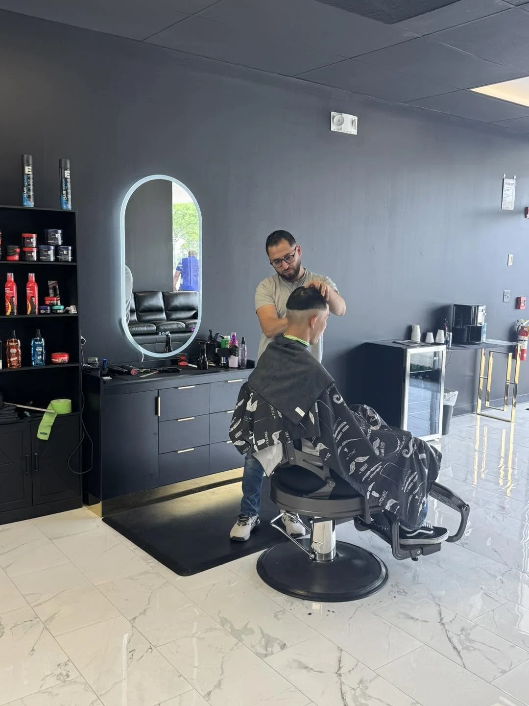 A barber working on a haircut at an illuminated mirror in Axis Cuts
