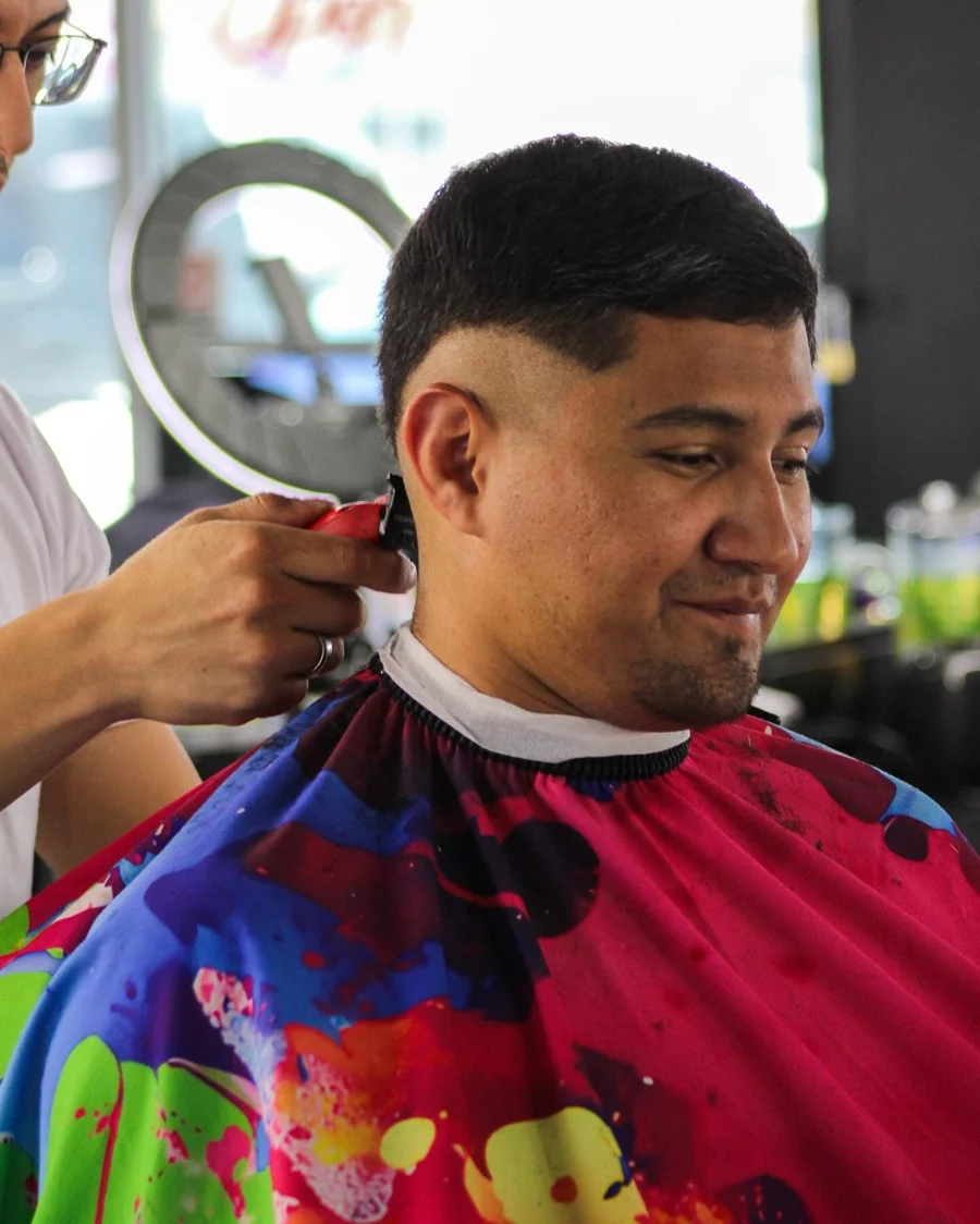 A barber working on an adult client's haircut inside Chingon Cuh’ts