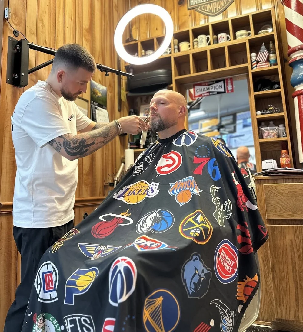 Barber grooming an adult client’s beard inside Damon’s wood-paneled shop