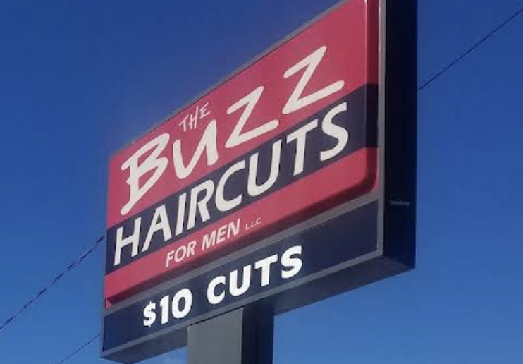 The raspberry-red roadside sign for The Buzz Haircuts For Men